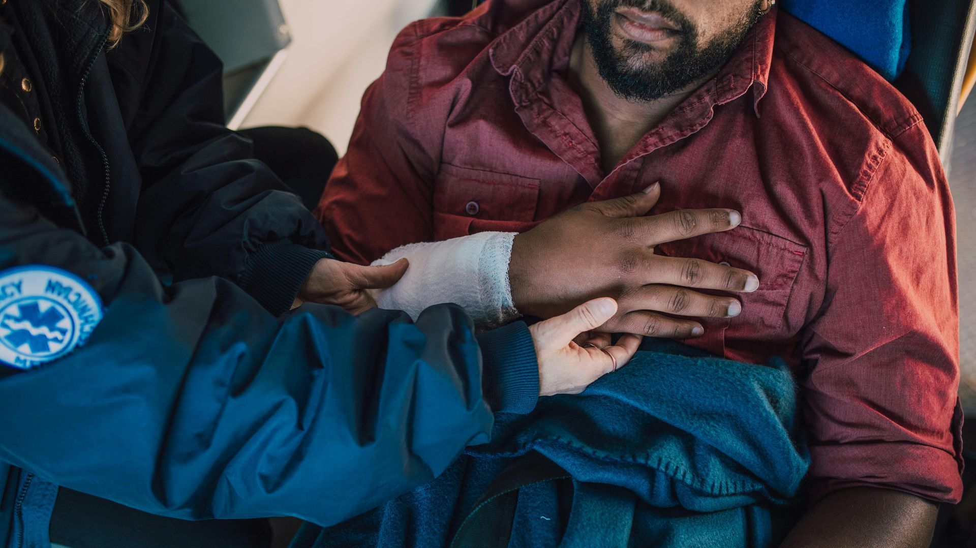 A man with a bandage on his arm is being helped by an ambulance driver.