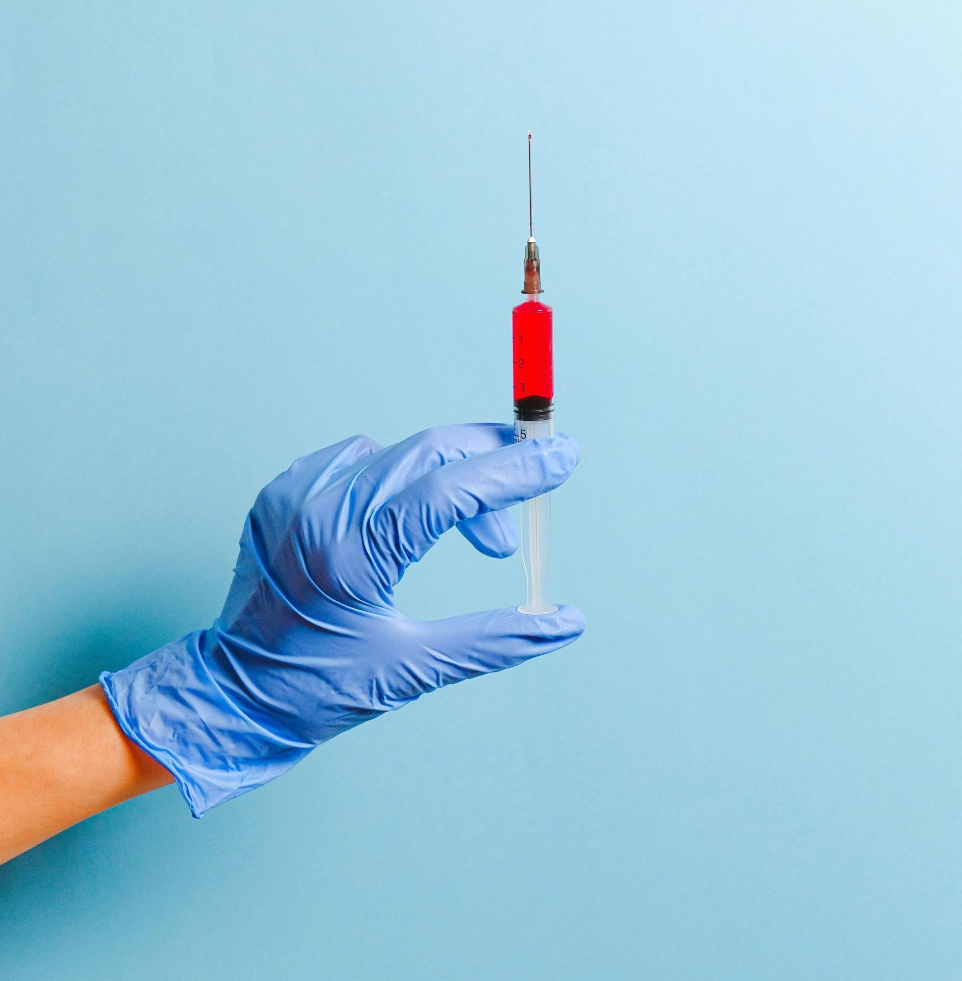 A person wearing blue gloves is holding a syringe with red liquid in it.