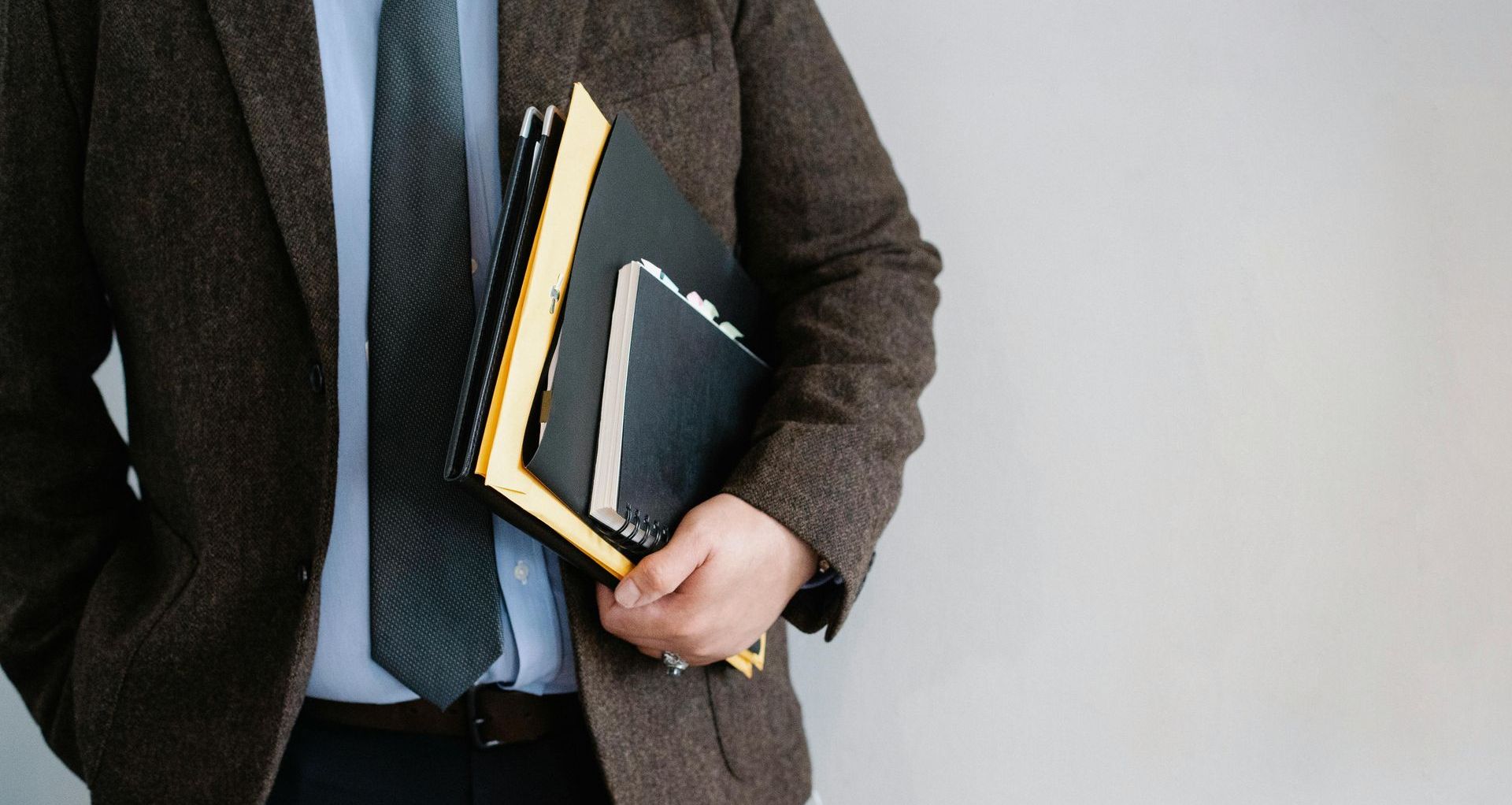 A man in a suit and tie is holding a stack of notebooks.