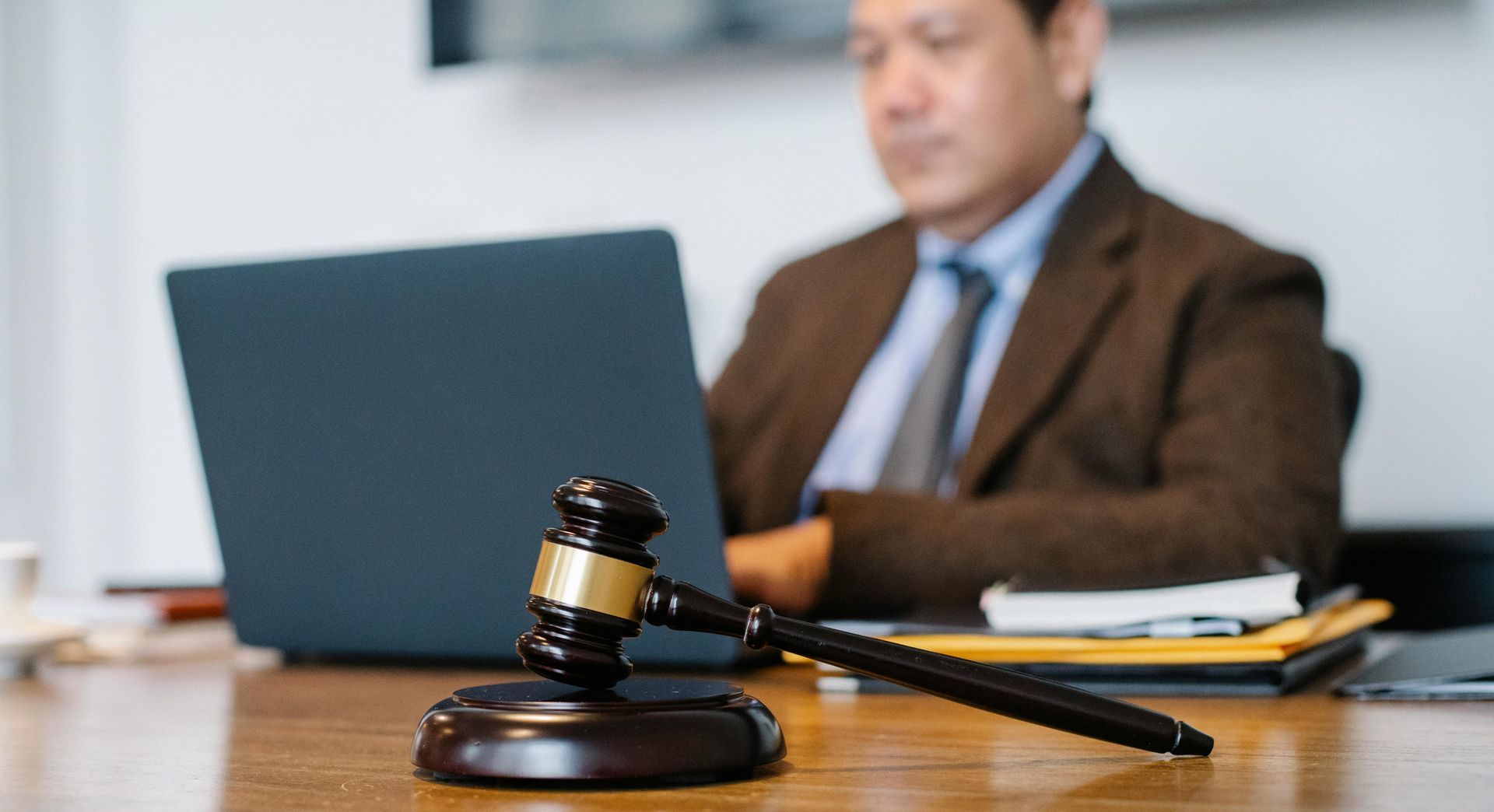 A man is sitting at a table with a laptop and a judge 's gavel.