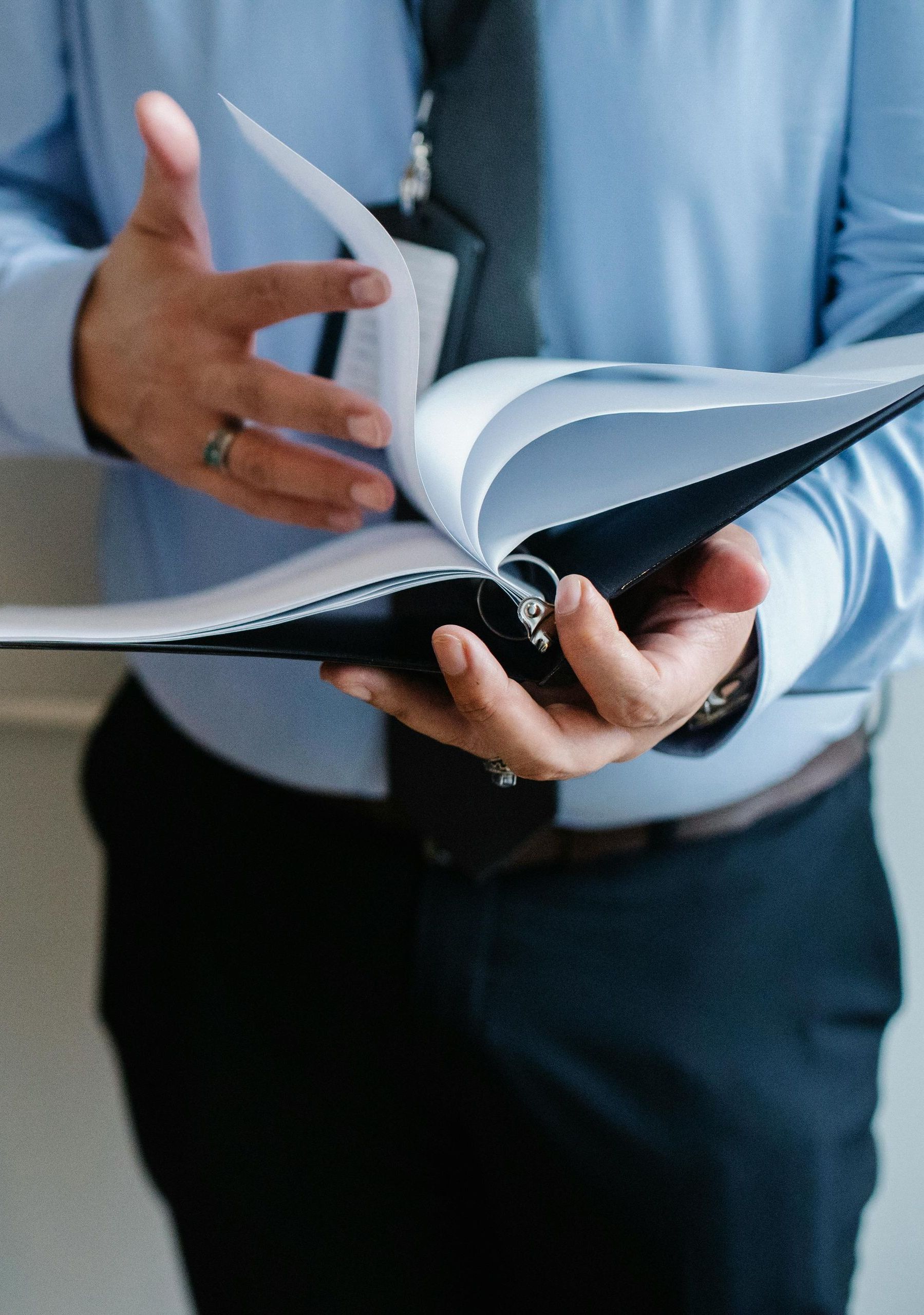 A man in a blue shirt and tie is holding a binder with papers in it.