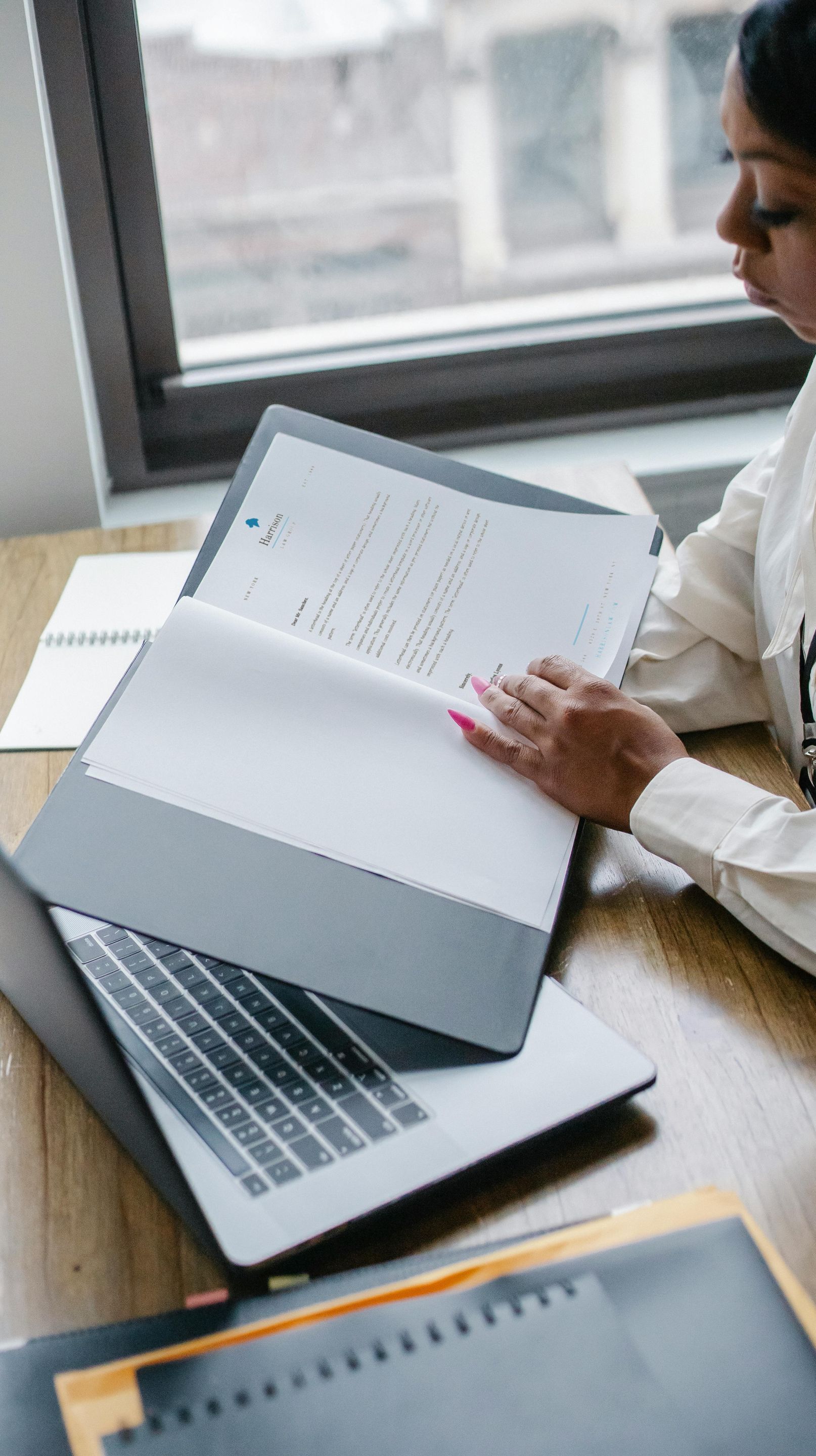 A woman is sitting at a desk with a laptop and papers.