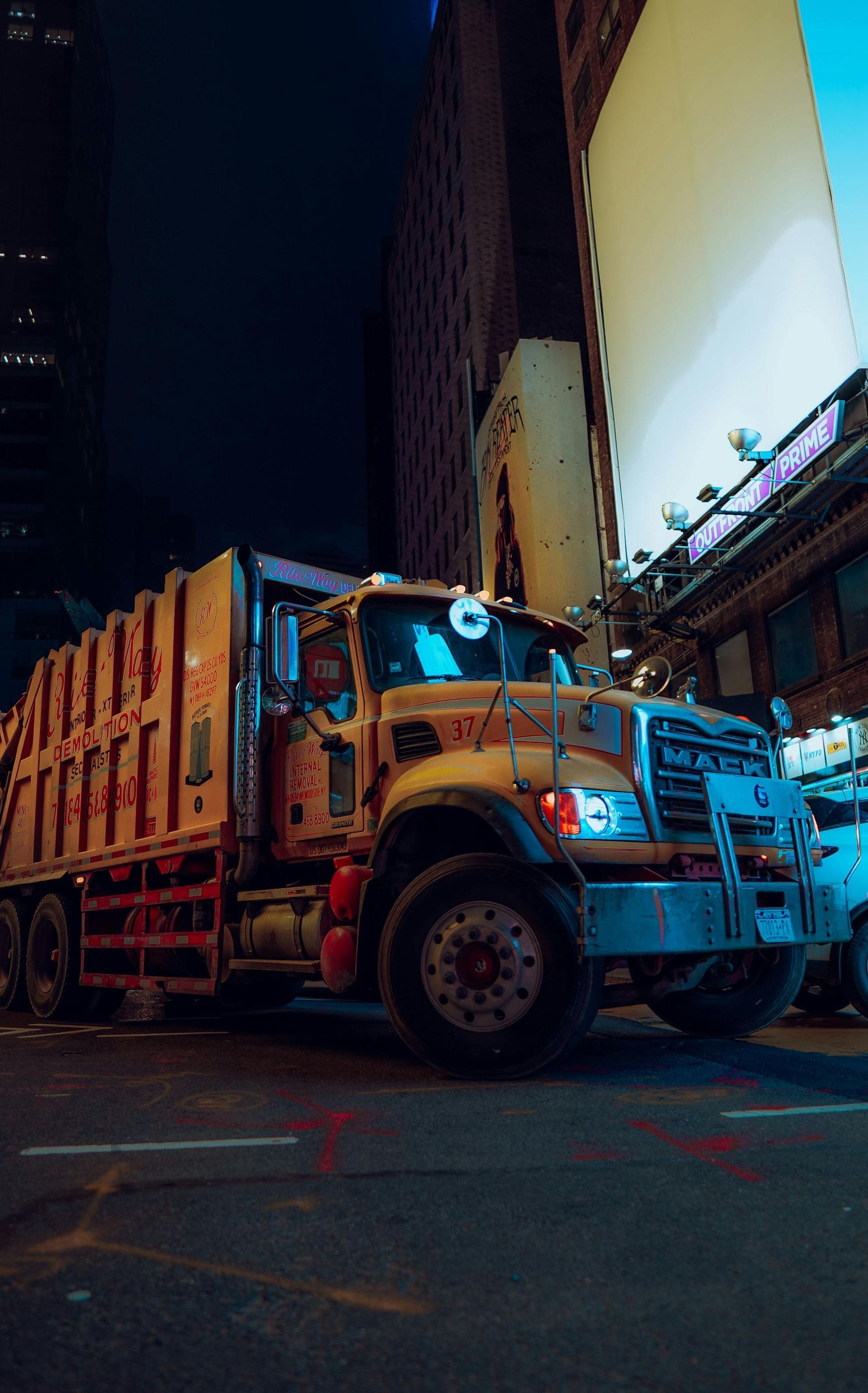 A garbage truck is parked on the side of a city street at night.