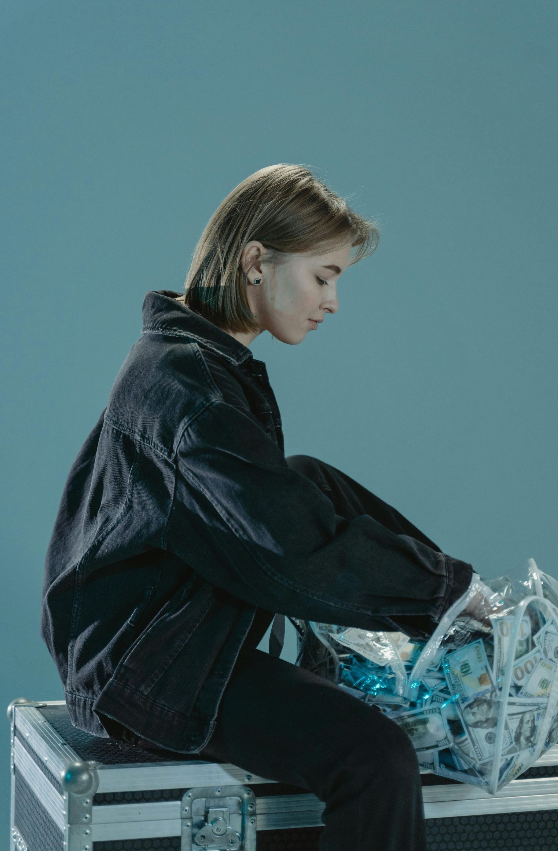 A woman in a black jacket is sitting on a suitcase.