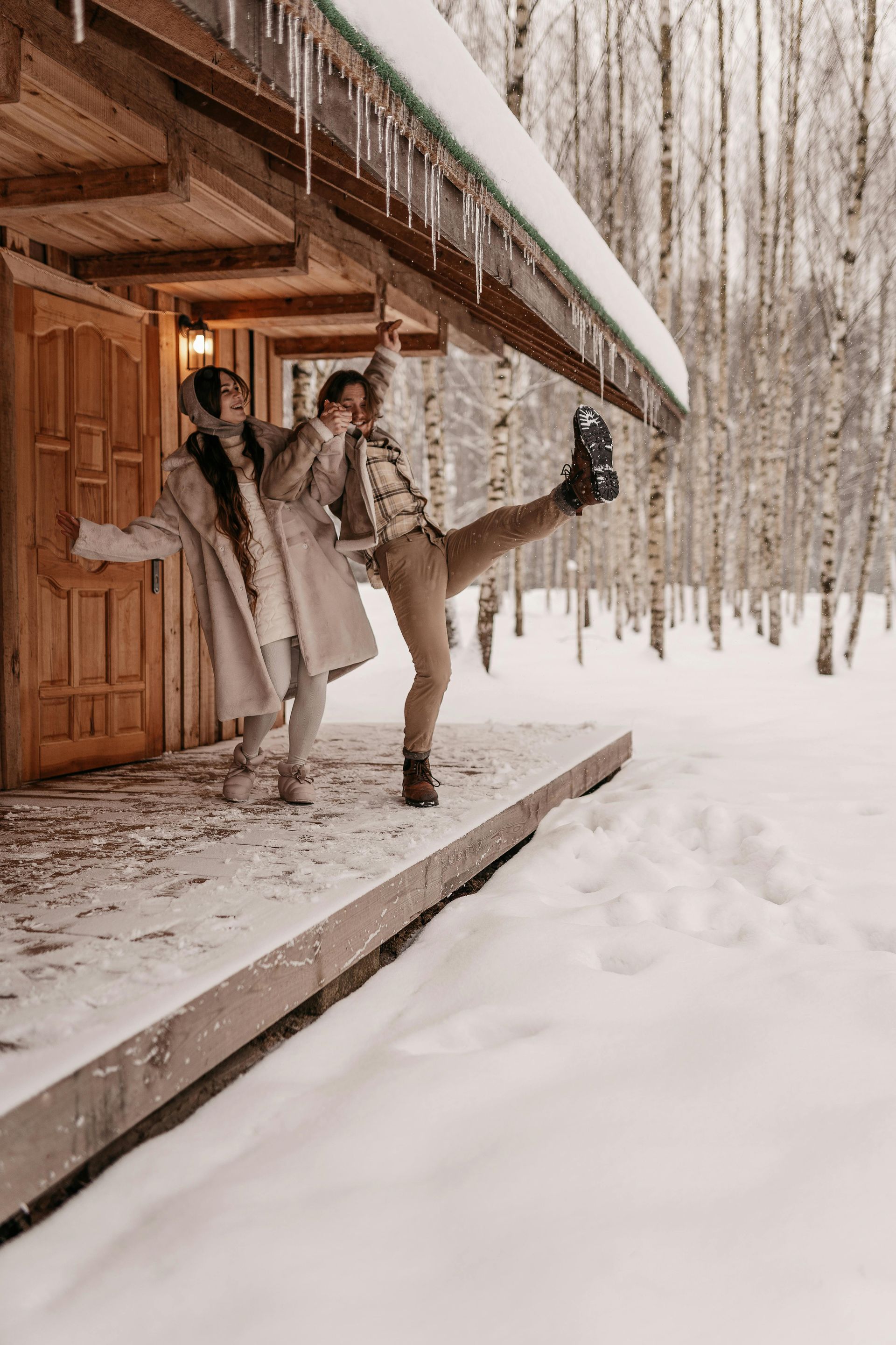 a man and a woman are standing on the porch of a cabin in the snow 