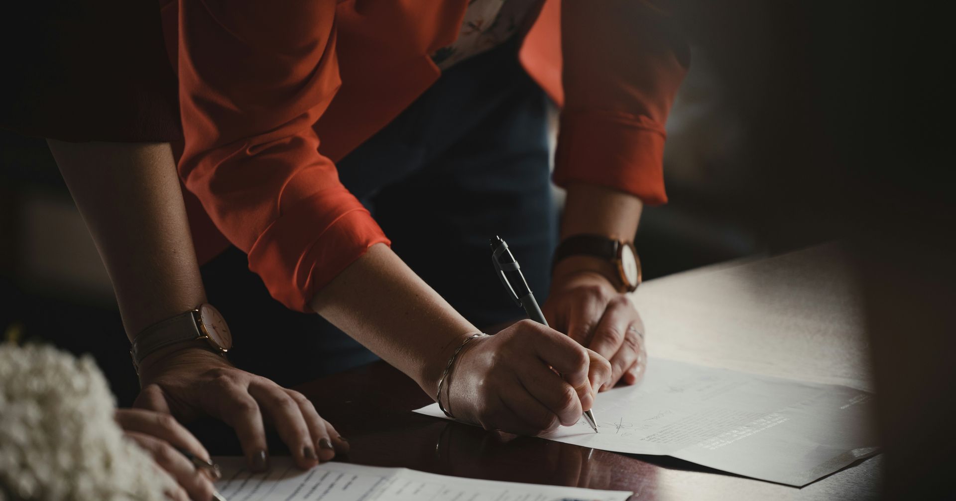 a woman is signing a document with a pen on a table.