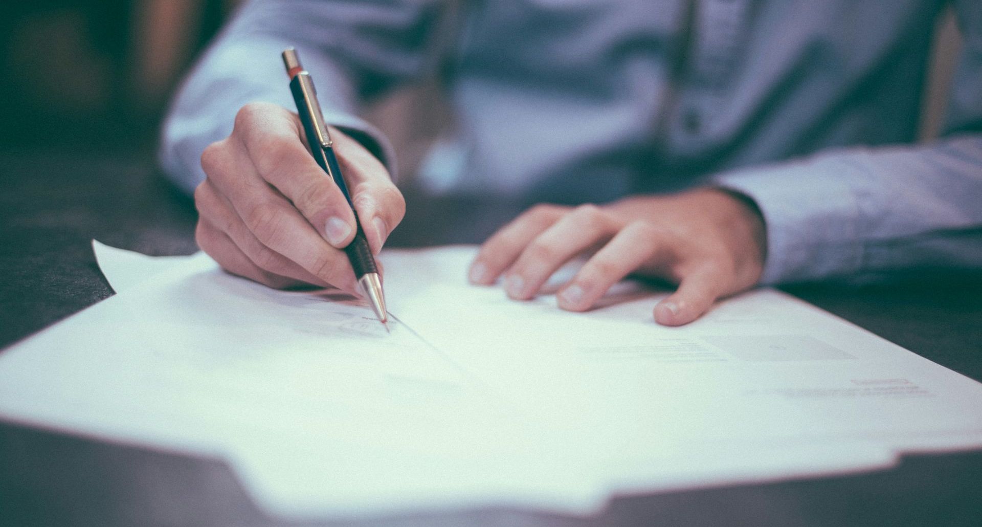 A man is writing on a piece of paper with a pen.
