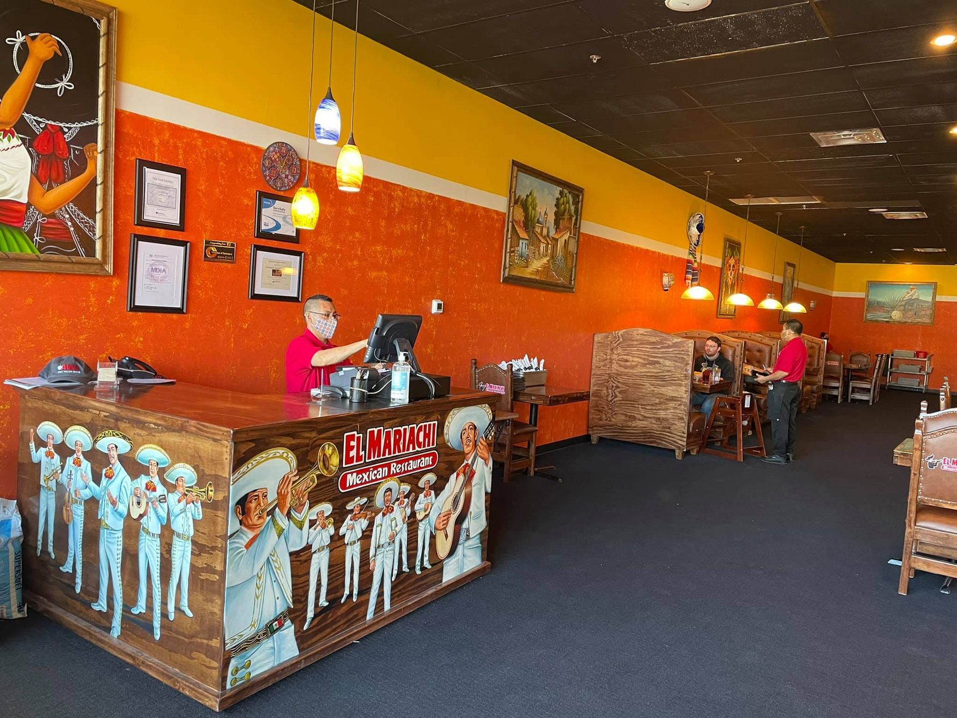 A brightly painted restaurant interior features a wooden counter decorated with a mariachi mural and orange walls.
