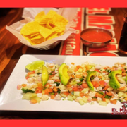 A white rectangular plate of ceviche topped with avocado slices, served with tortilla chips, salsa, and a drink.