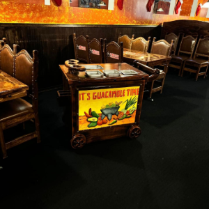A room with tables holding numerous white gift bags, a world map on the wall, and a television playing a sports game.