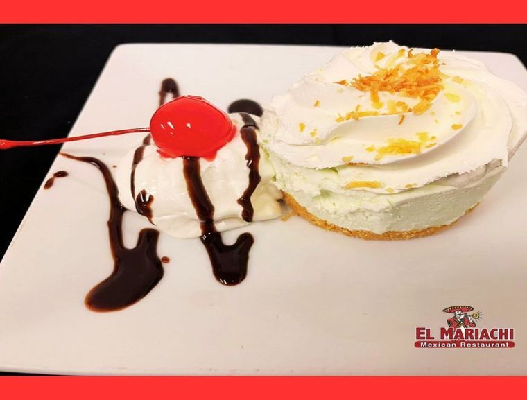A dessert plate with a light green pie topped with whipped cream and zest, plus a cherry with whipped cream and syrup.
