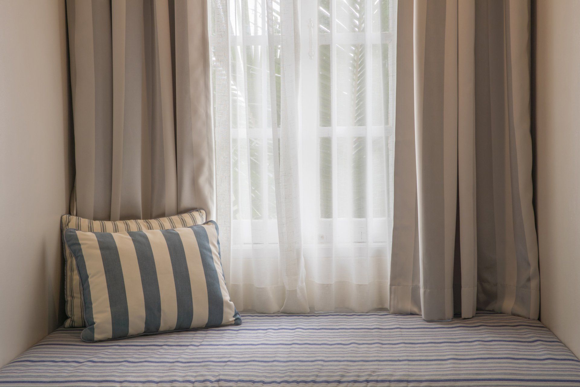 Close up of window with cushions in sitting space, drapes pulled back to show white sheers behind.