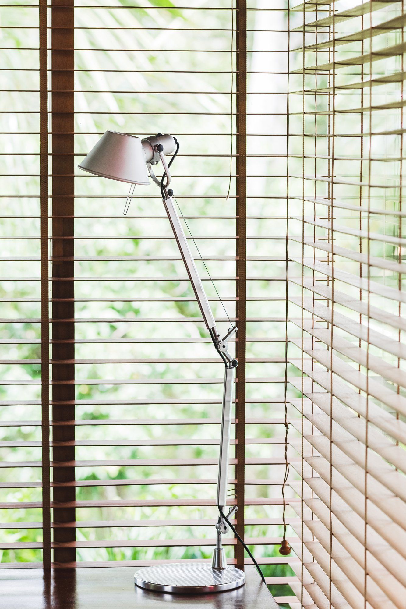 Close up of metal lamp on desk, in corner of room with open timber venetian blinds.