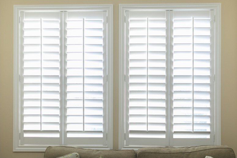 Dual white plantation shutters, slightly open, letting light shine in through window against yellow walls.
