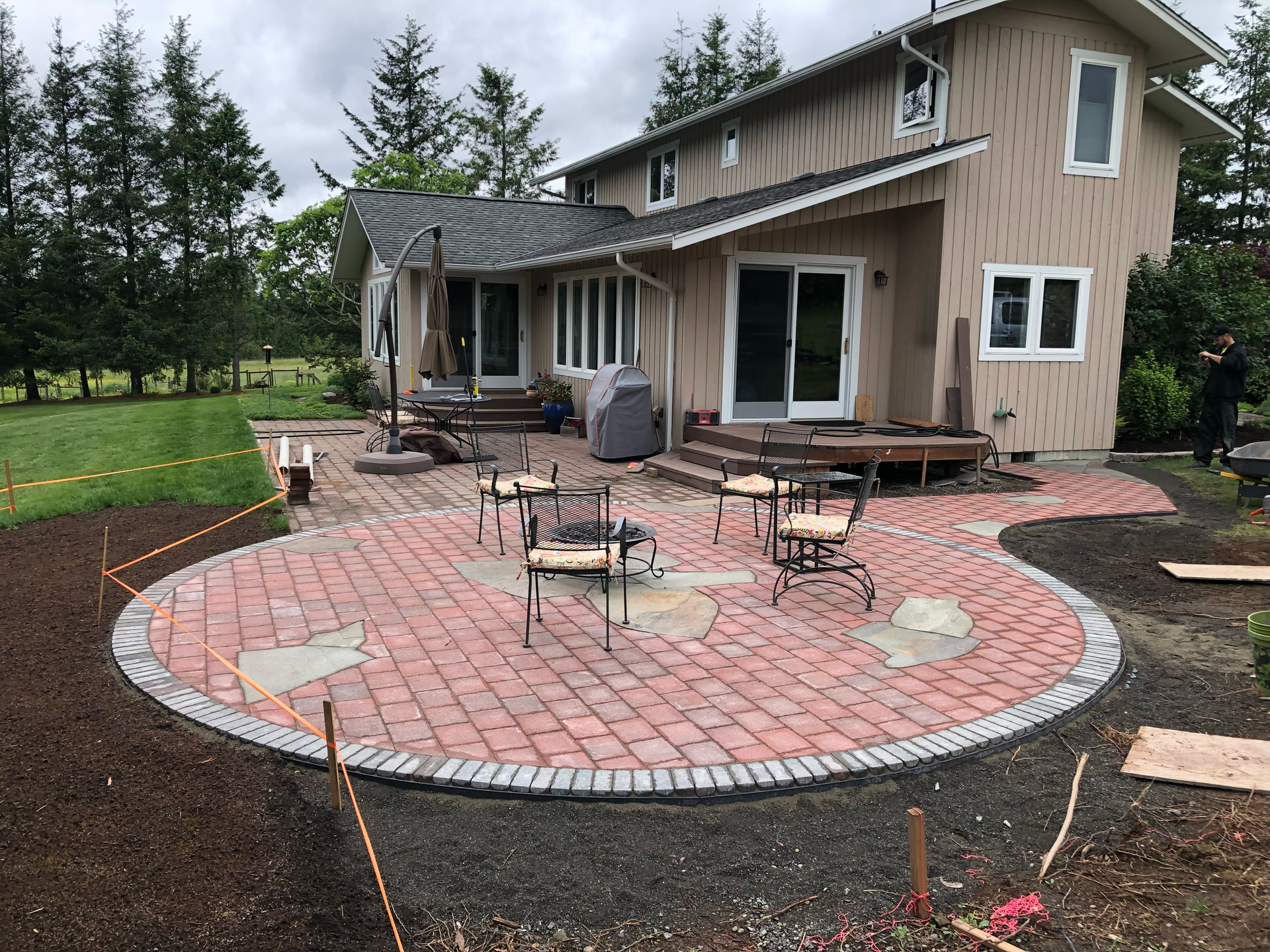 Backyard patio with red pavers, outdoor chairs, and a beige two-story house with a covered deck.