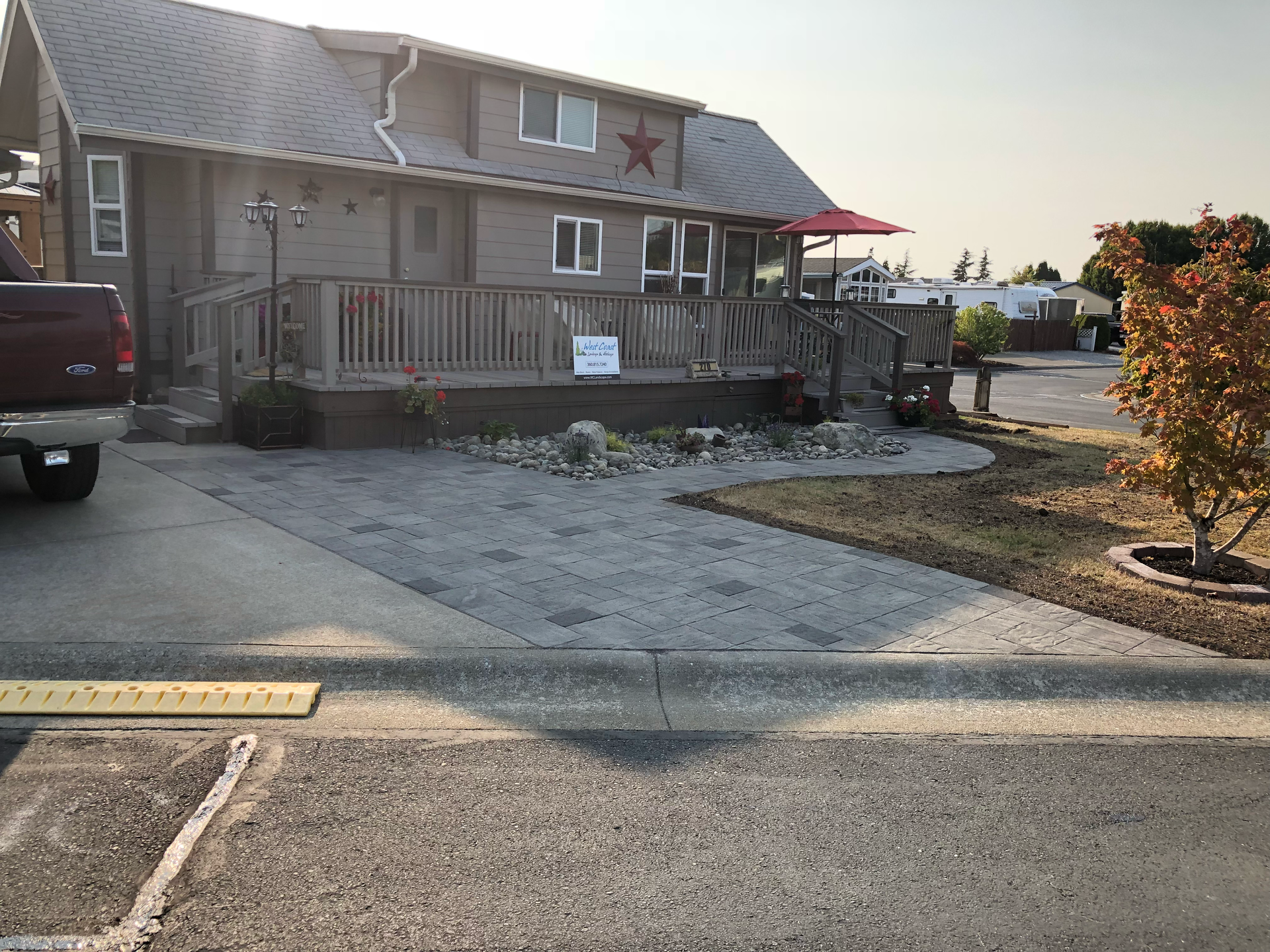 House with wooden porch and gravel driveway at sunset, with parked truck and landscaped yard.