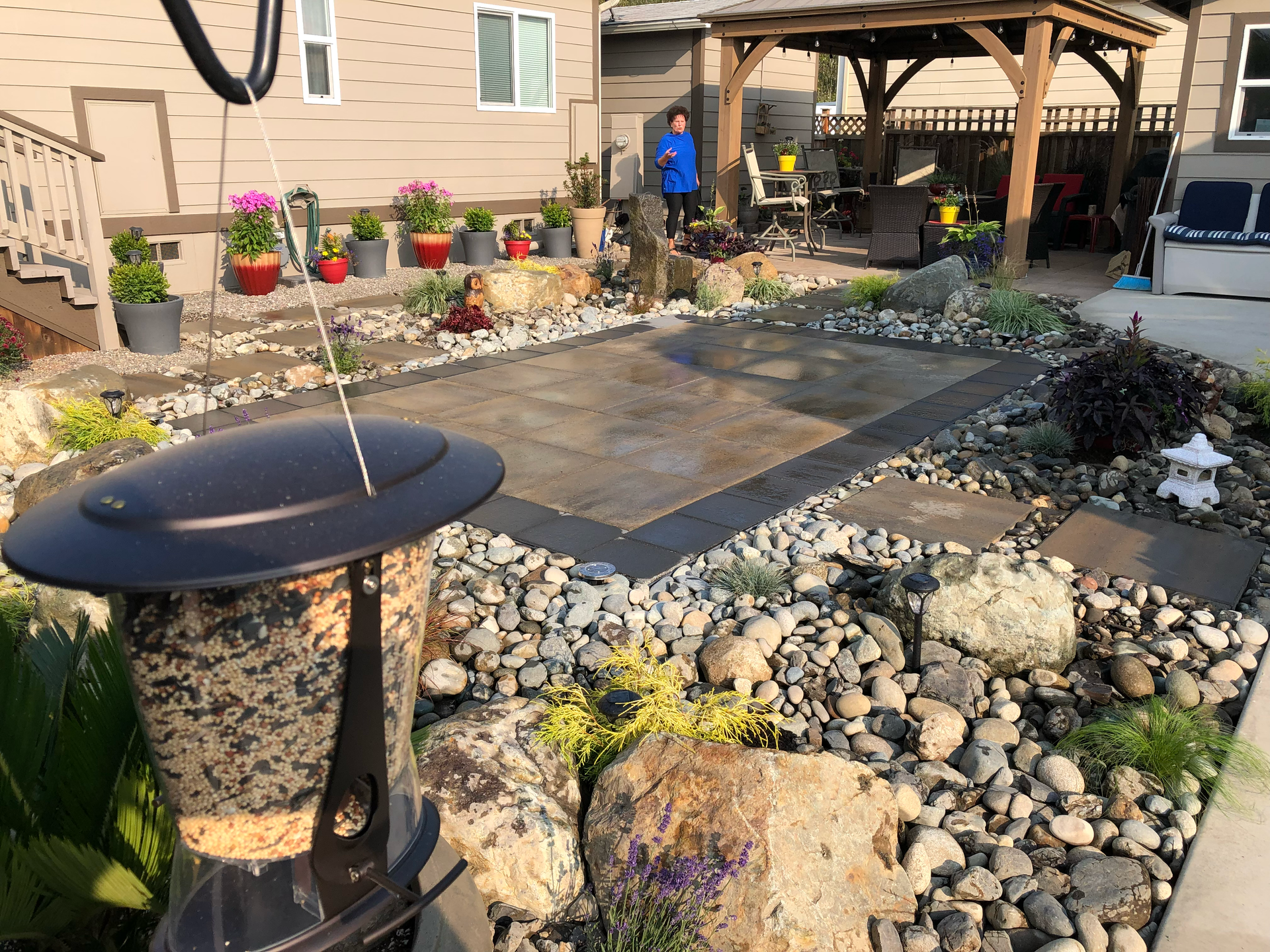 Backyard patio with stone pavers, decorative rocks, and a gazebo under a sunny sky