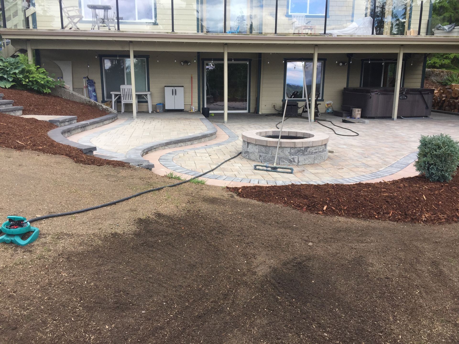 Patio with a stone fire pit, curved bench, and sliding glass doors beside a mulch-covered yard.
