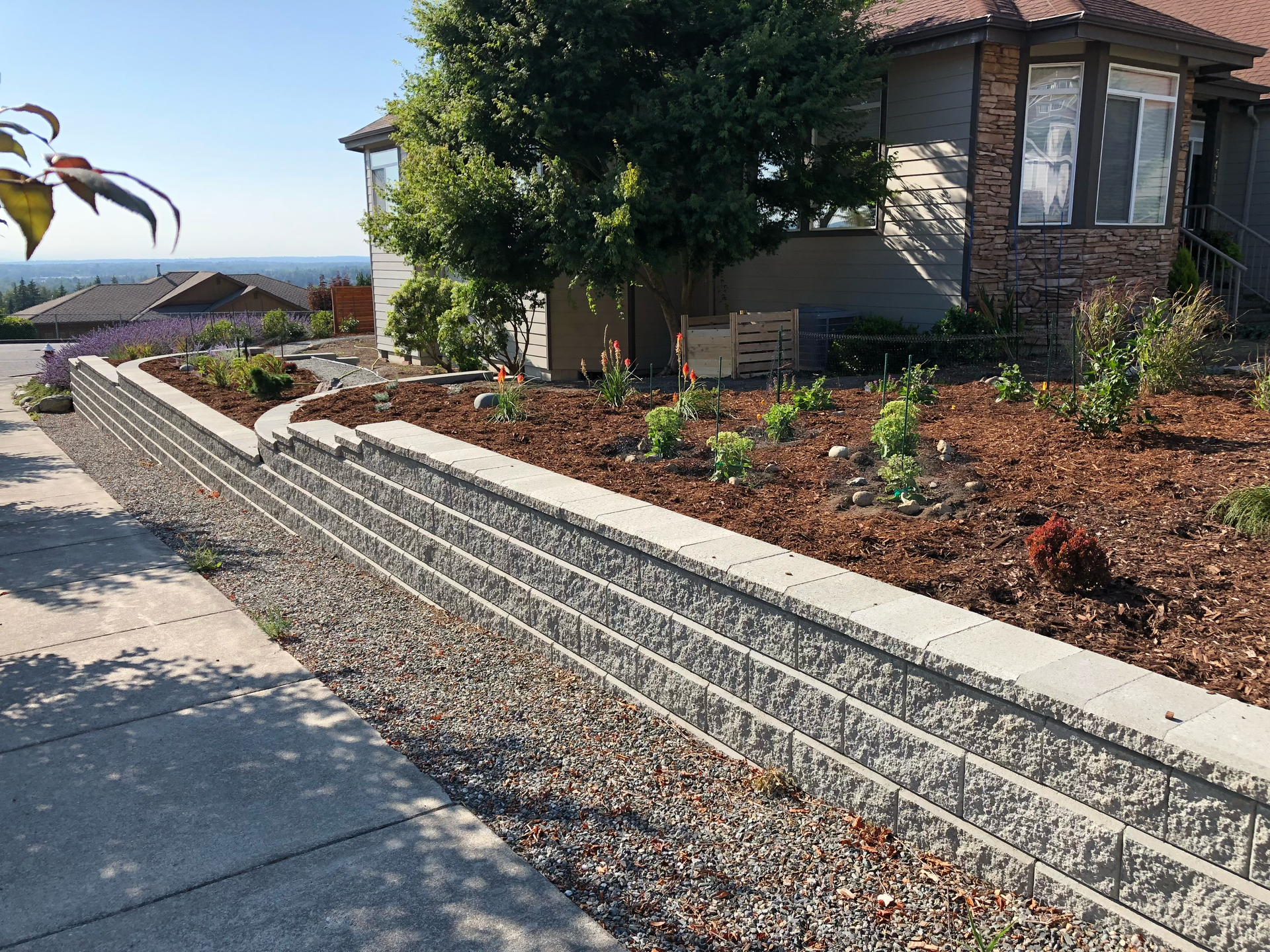 Landscaped front yard with terraced stone retaining wall beside a concrete driveway and house.