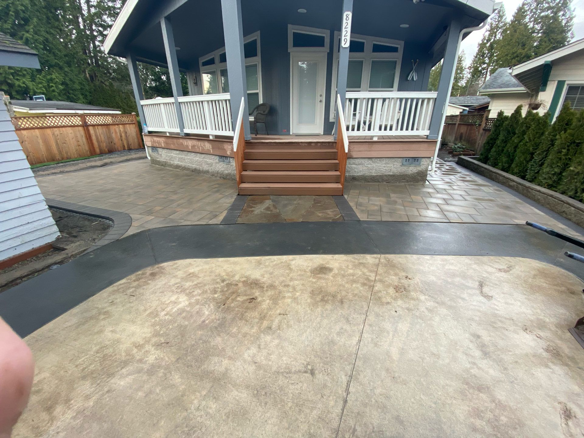 Front porch of a house with wooden steps, white railing, and a paved driveway in the foreground.