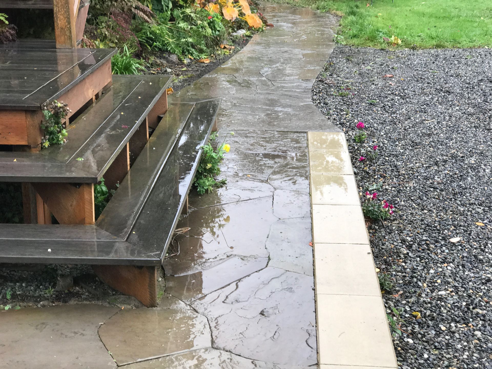 Wet stone garden path beside wooden steps and gravel bed