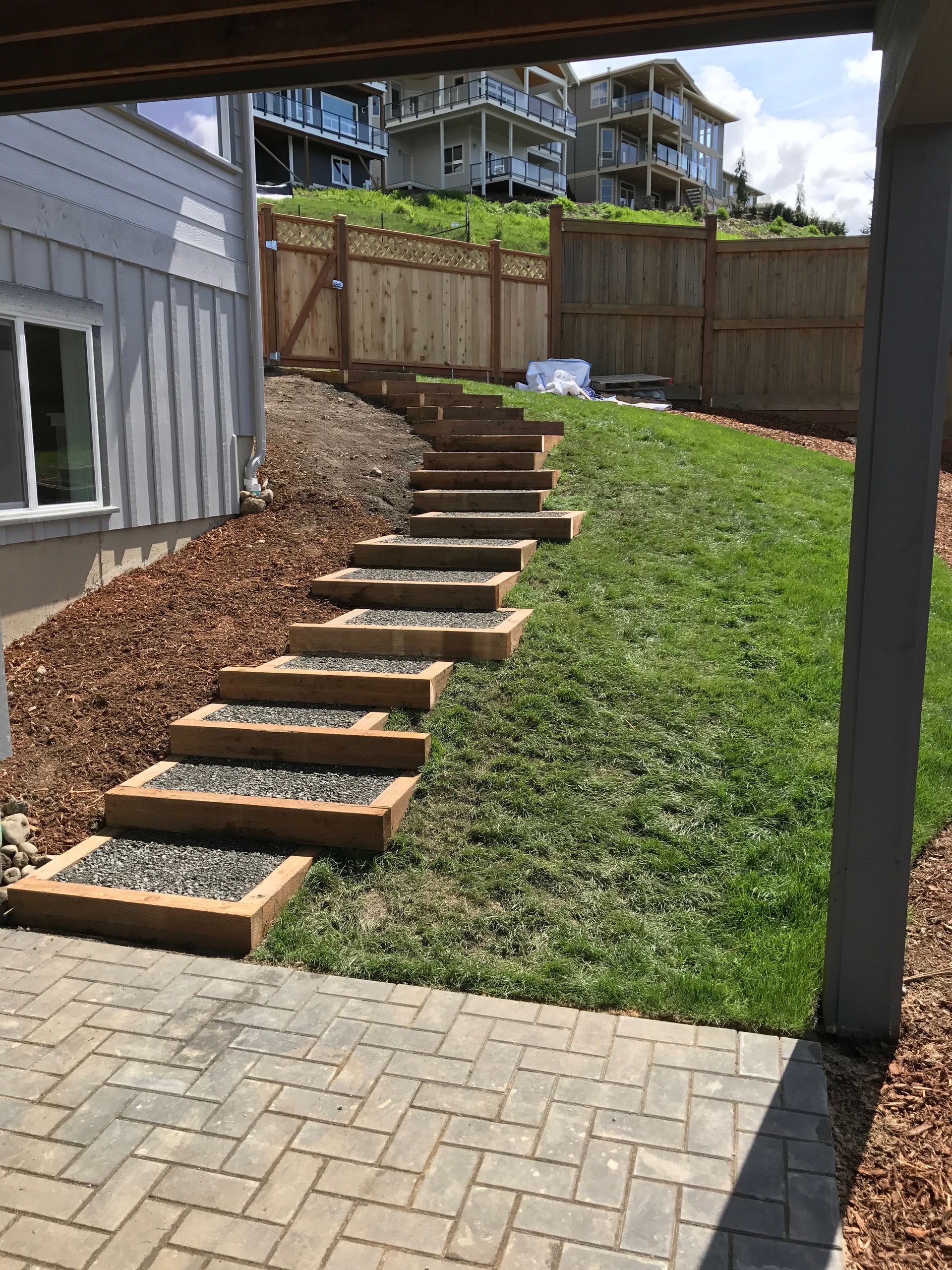 Backyard with staggered wooden steps up a grassy slope beside a fence and retaining wall