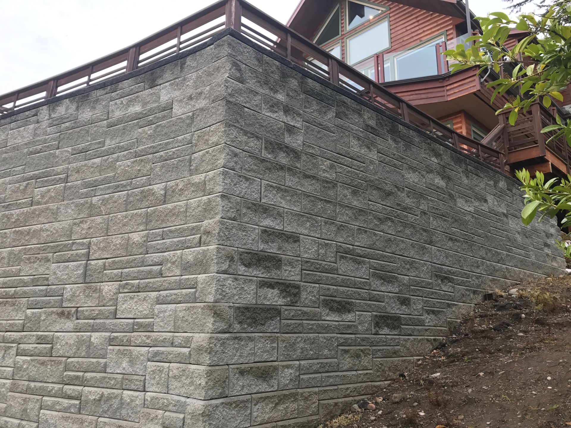 Stone retaining wall beside a sloped path, with a wooden building visible above it