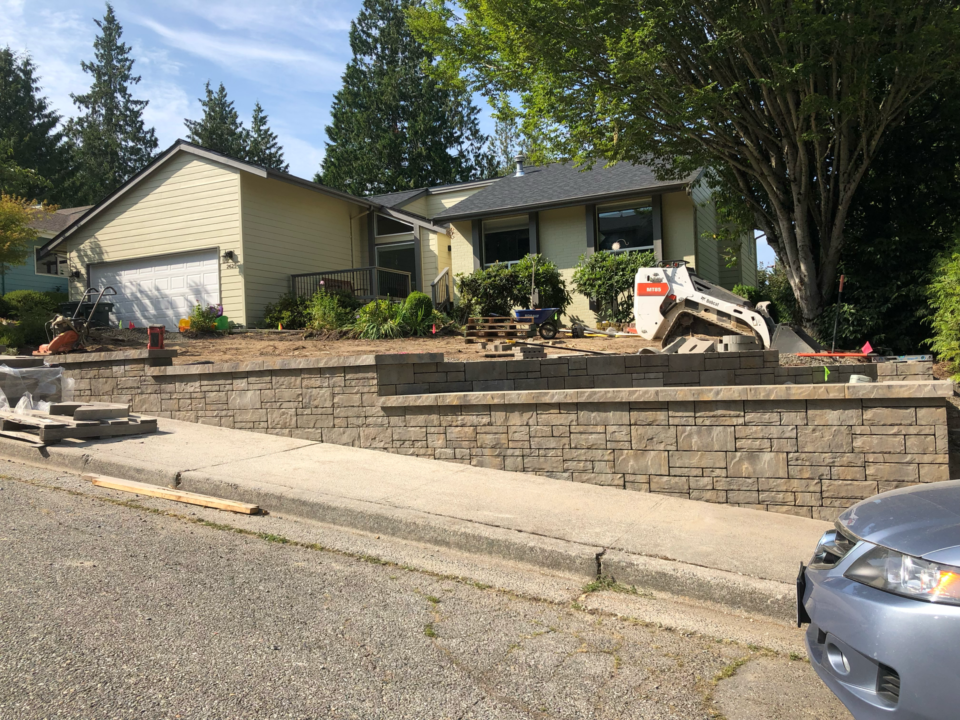 Residential house with stone retaining wall and small excavator by the driveway