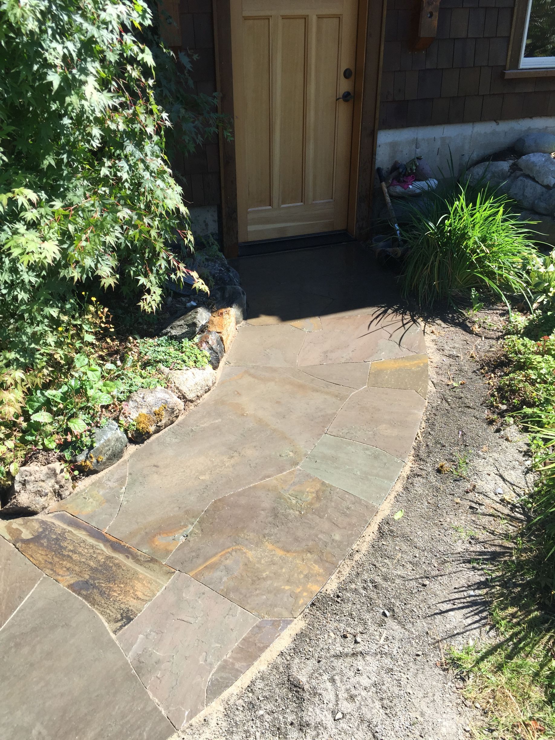 Stone walkway leading to a wooden front door beside garden plants and gravel path