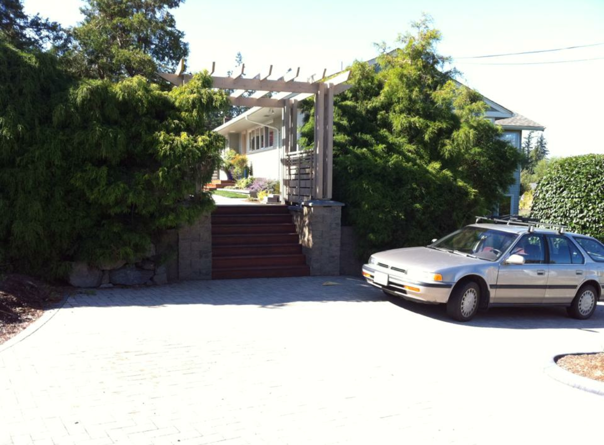 House entrance with stone steps and a parked silver sedan in front, surrounded by trees and shrubs
