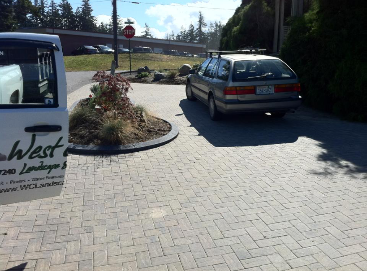 Paved driveway with parked silver station wagon beside a landscaped entrance and white van.