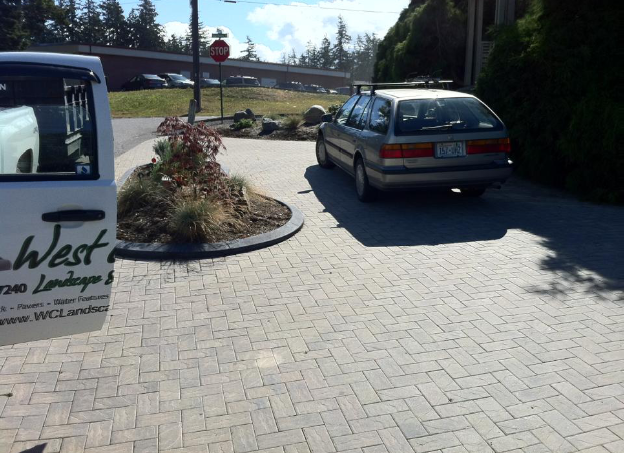Parked minivan on a sunlit paved driveway beside a landscaped island and signpost.