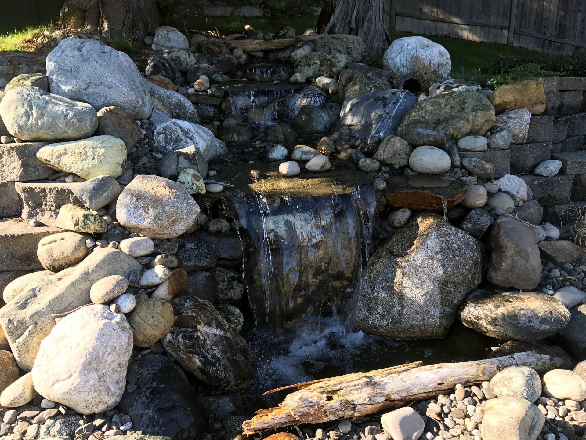 Small stone waterfall flowing over rocks in a garden pond.