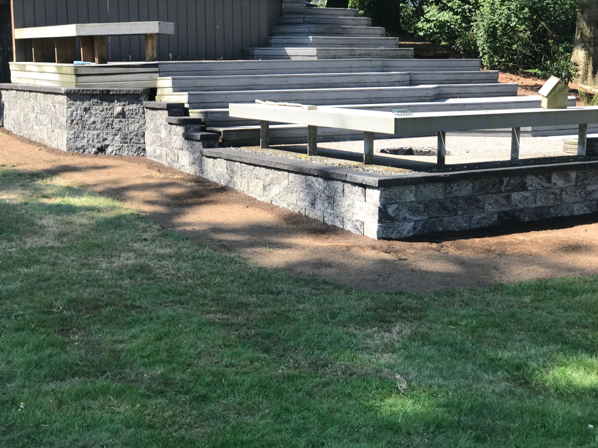 Stone patio steps and raised seating platforms beside a grassy yard in sunlight