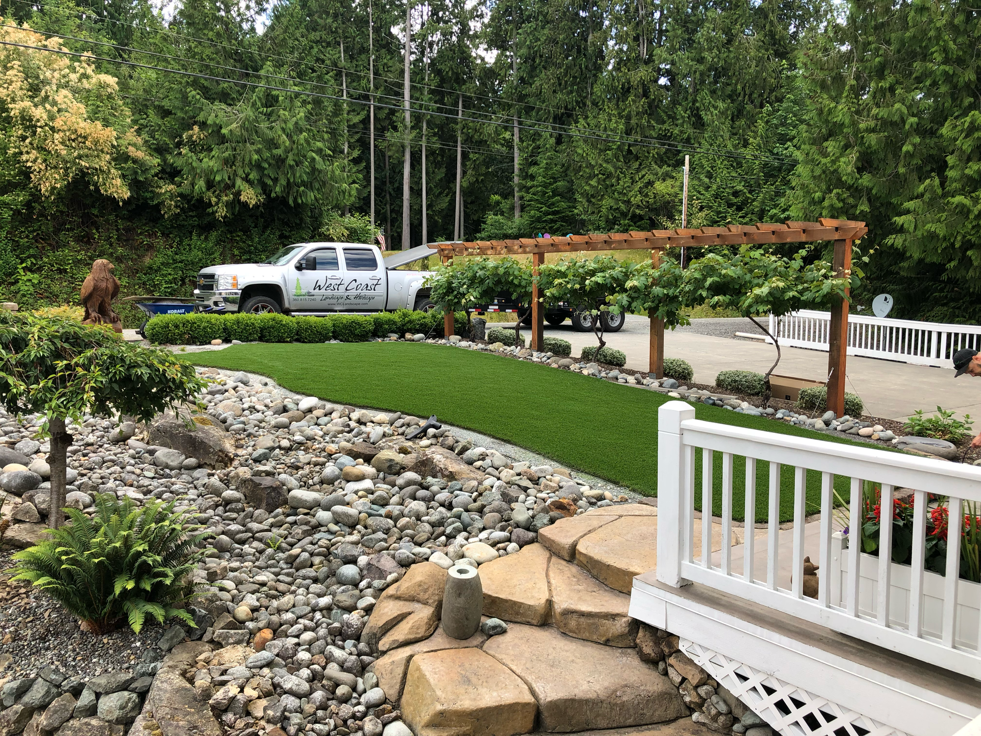 Landscaped garden with stone path, white railing, and a white pickup truck near a pergola.