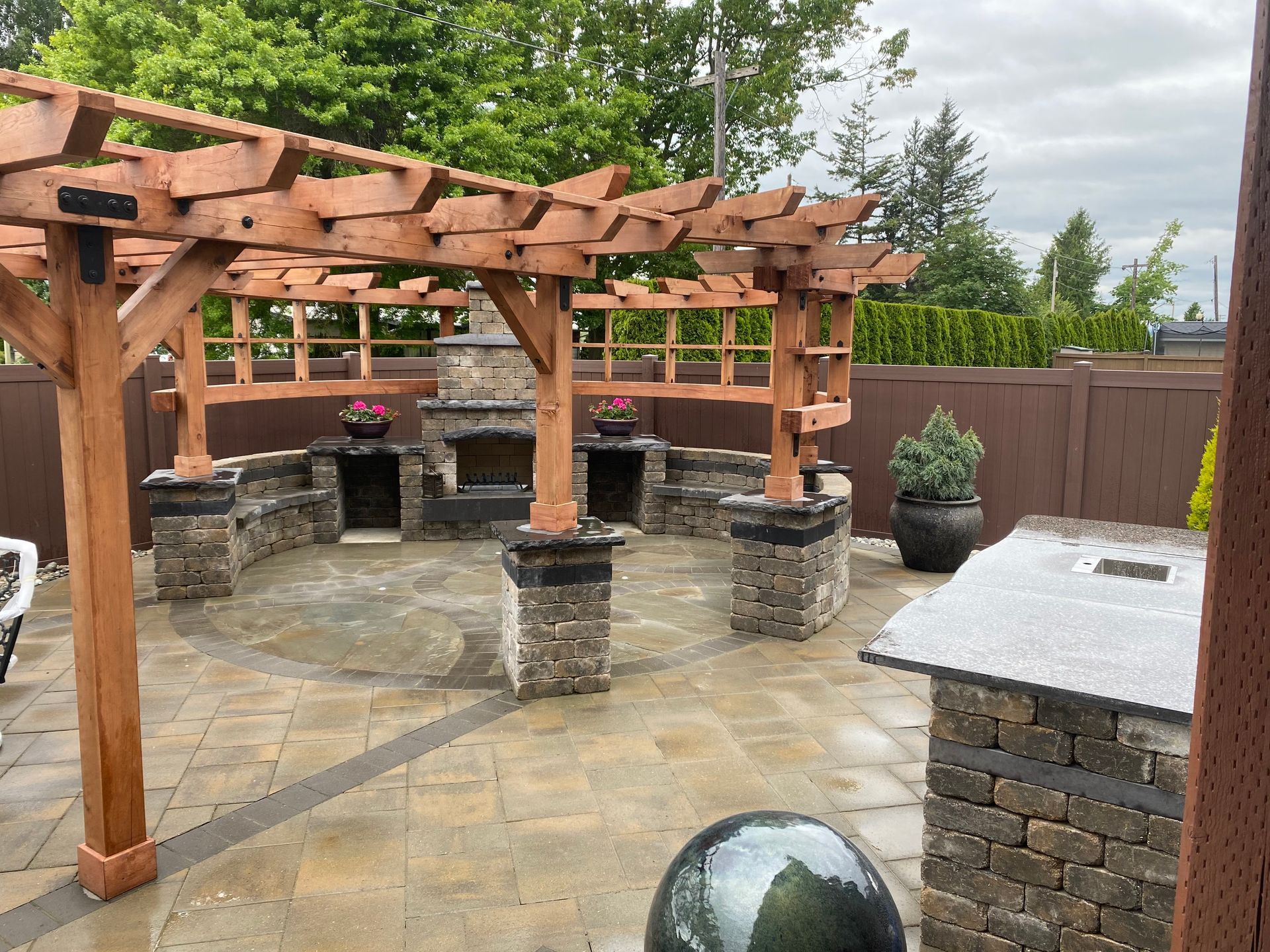 Backyard patio with wooden pergola, stone pillars, grill, and stone seating area