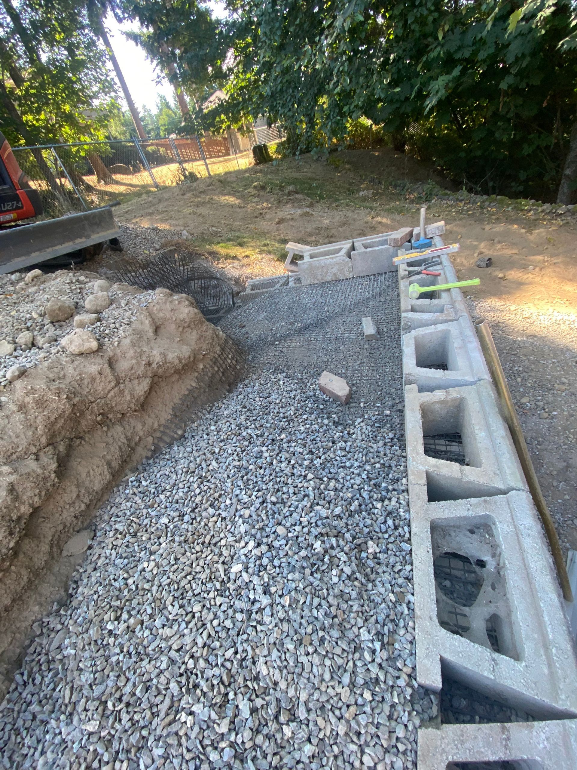 Gravel walkway under construction beside a cinder block retaining wall and dirt trench in a wooded yard