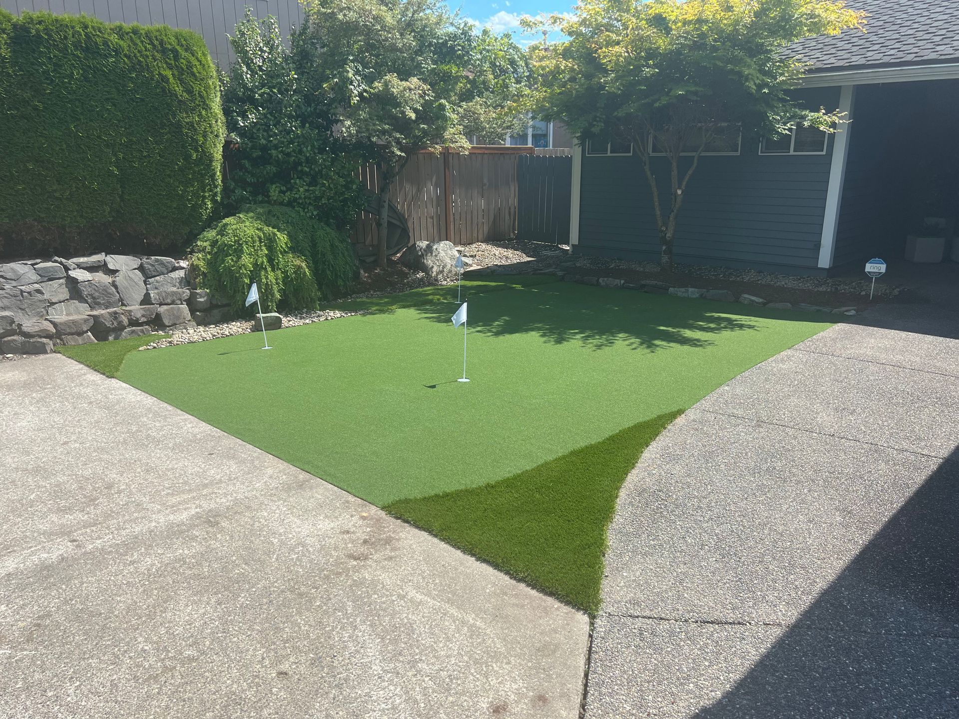 Backyard with artificial grass, stone paths, and hedges in bright sunlight