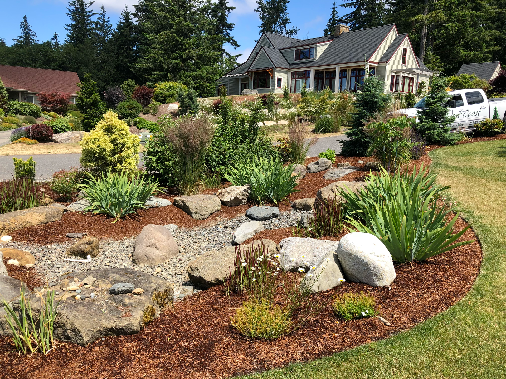 Landscaped front yard with rocks, shrubs, and mulch in front of a house under a clear blue sky