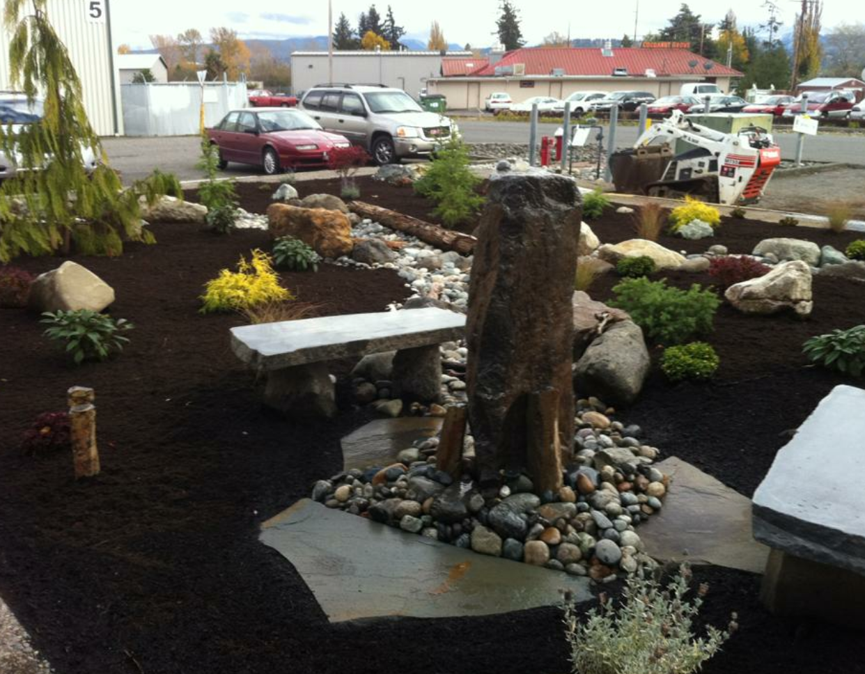 Landscaped garden with stone benches, rocks, and a tree stump centerpiece outdoors on a cloudy day