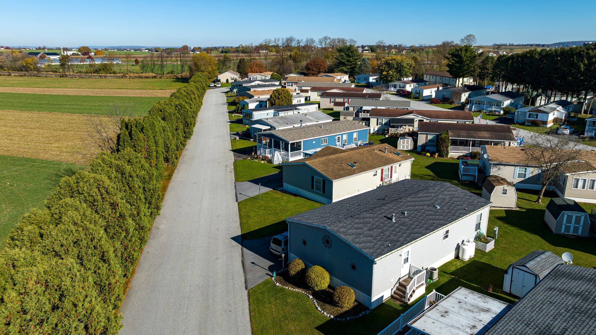 Aerial view of a suburban neighborhood beside open fields and a long tree-lined road.
