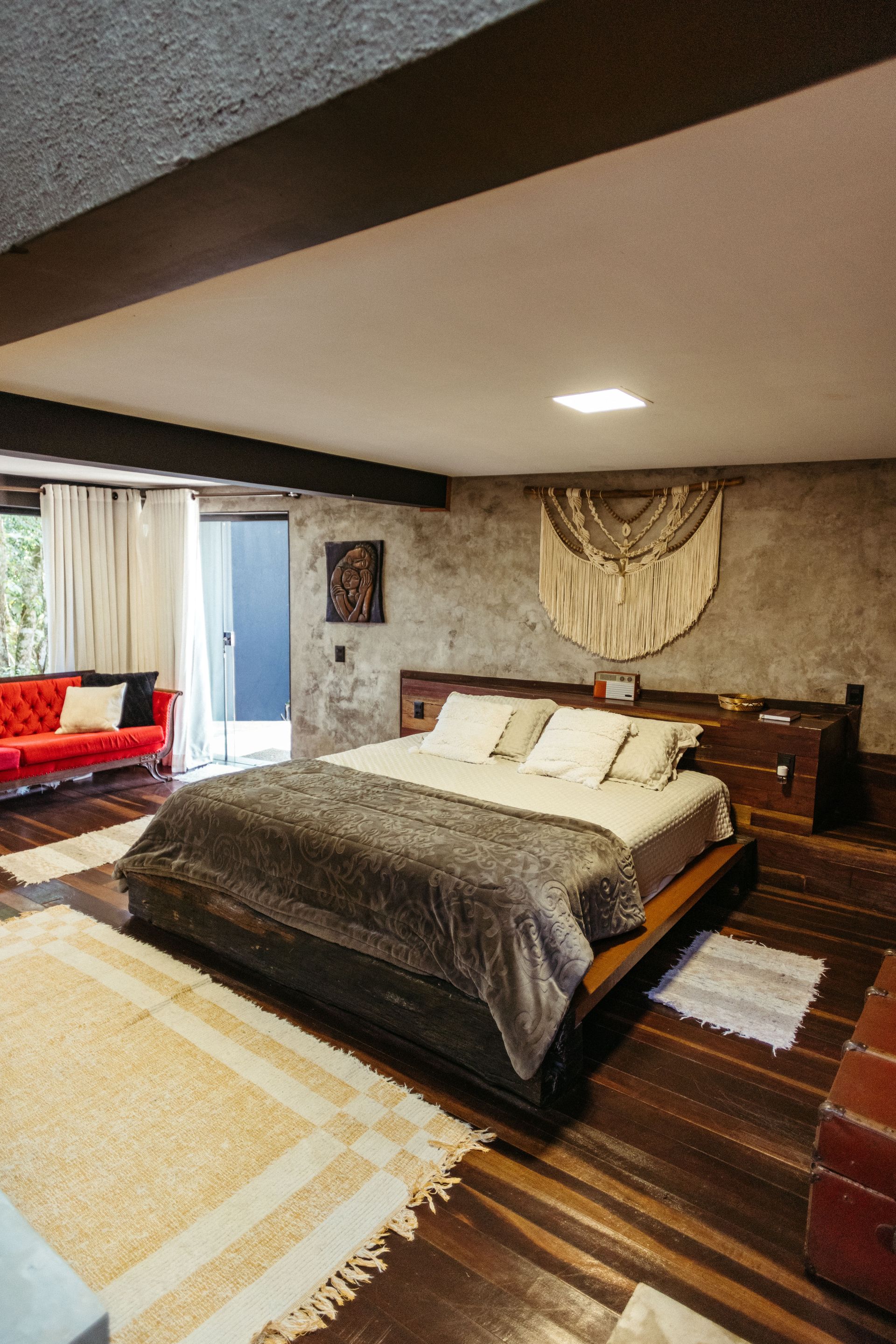 Quarto com cama grande, piso de madeira, parede com detalhes em pedra e portas de correr que dão para um pátio.