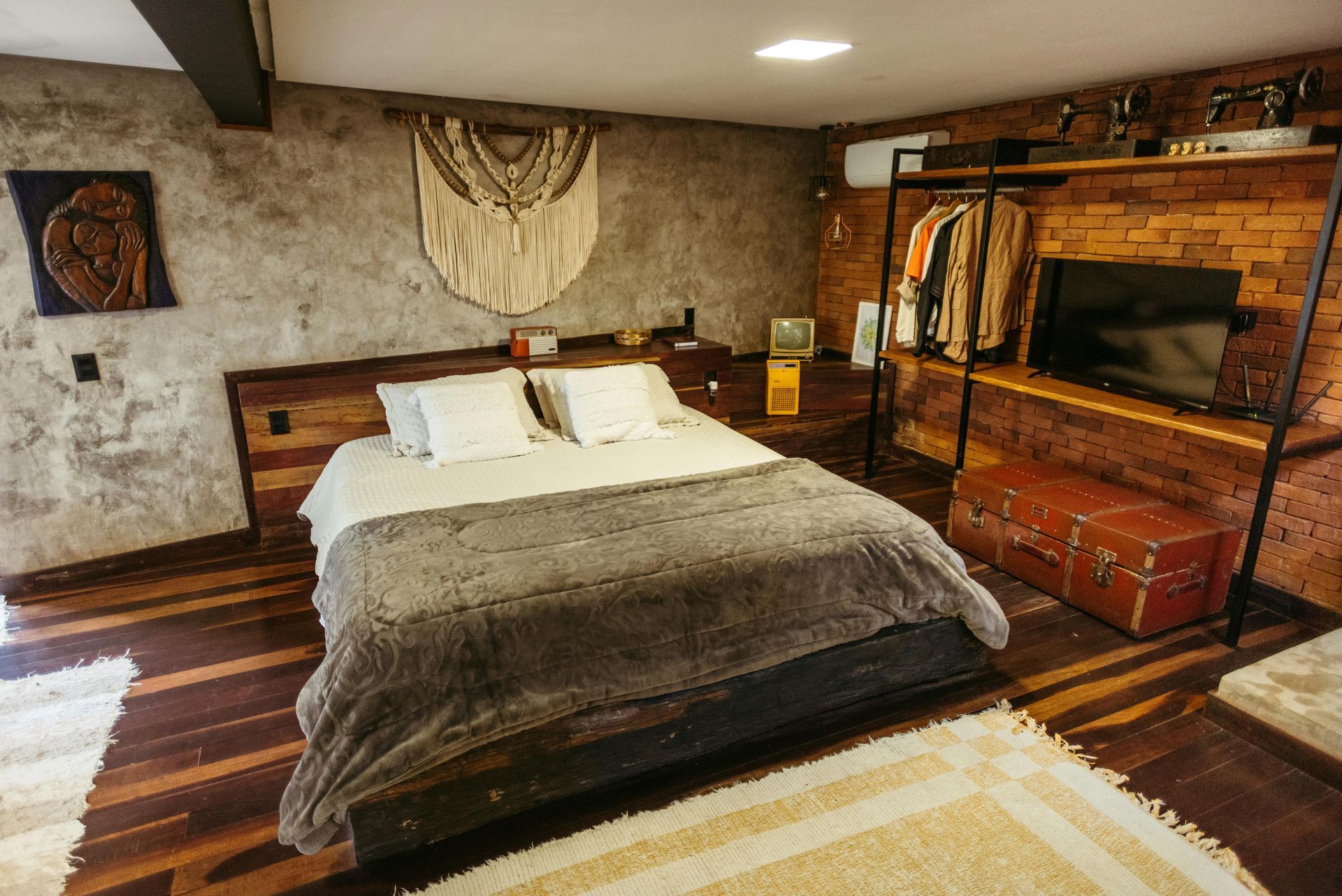 Quarto aconchegante com cama grande, lareira de tijolos, detalhes rústicos em madeira e iluminação acolhedora.