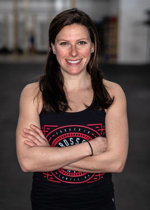 Smiling woman with crossed arms in a black tank top, standing in a gym-like setting