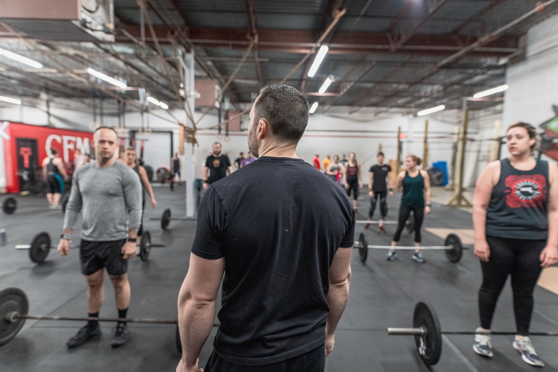 Group of people doing a barbell workout in an industrial-style gym, viewed from behind the instructor