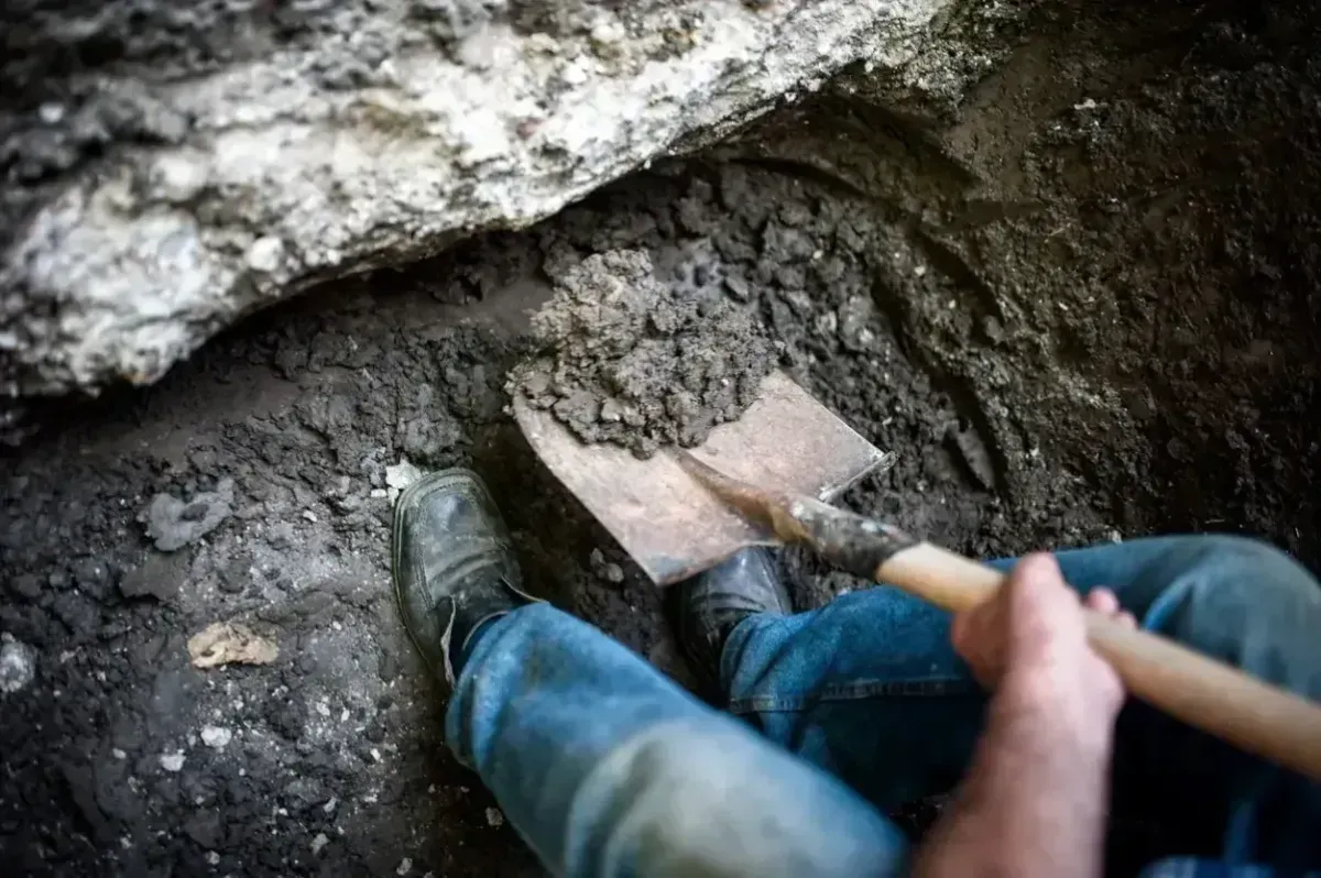 Person digging in dirt with a shovel in a rocky pit