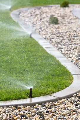 Gardener kneels on landscape fabric, hammering stakes around a garden hose in a landscaped bed.