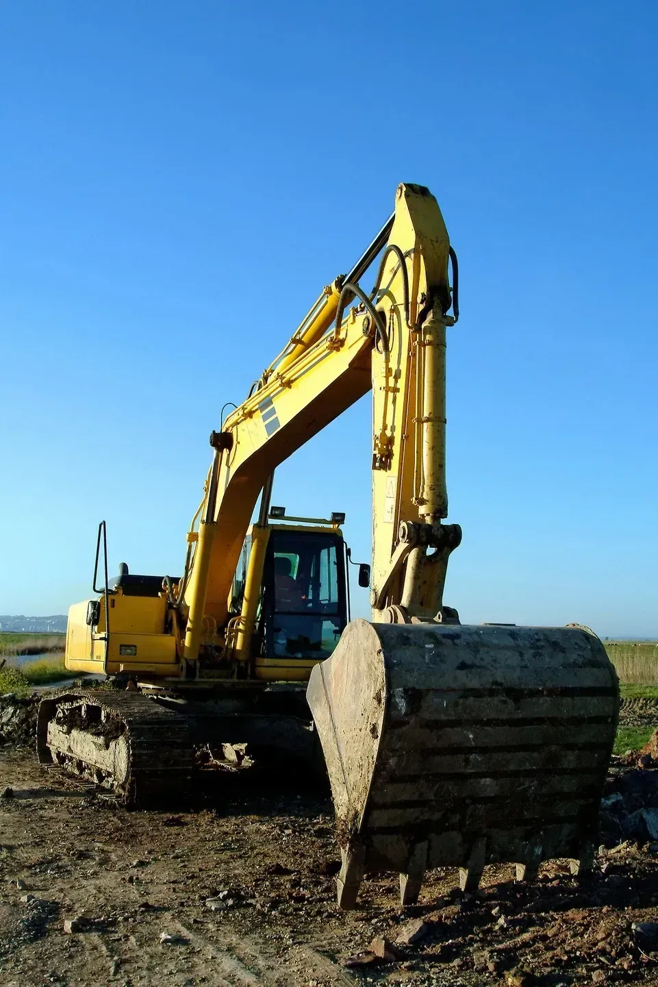 Yellow excavator on a muddy construction site under a clear blue sky
