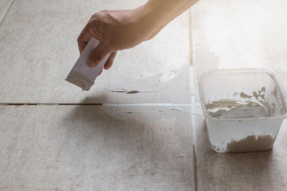 A person is applying grout to a tile floor with a spatula.