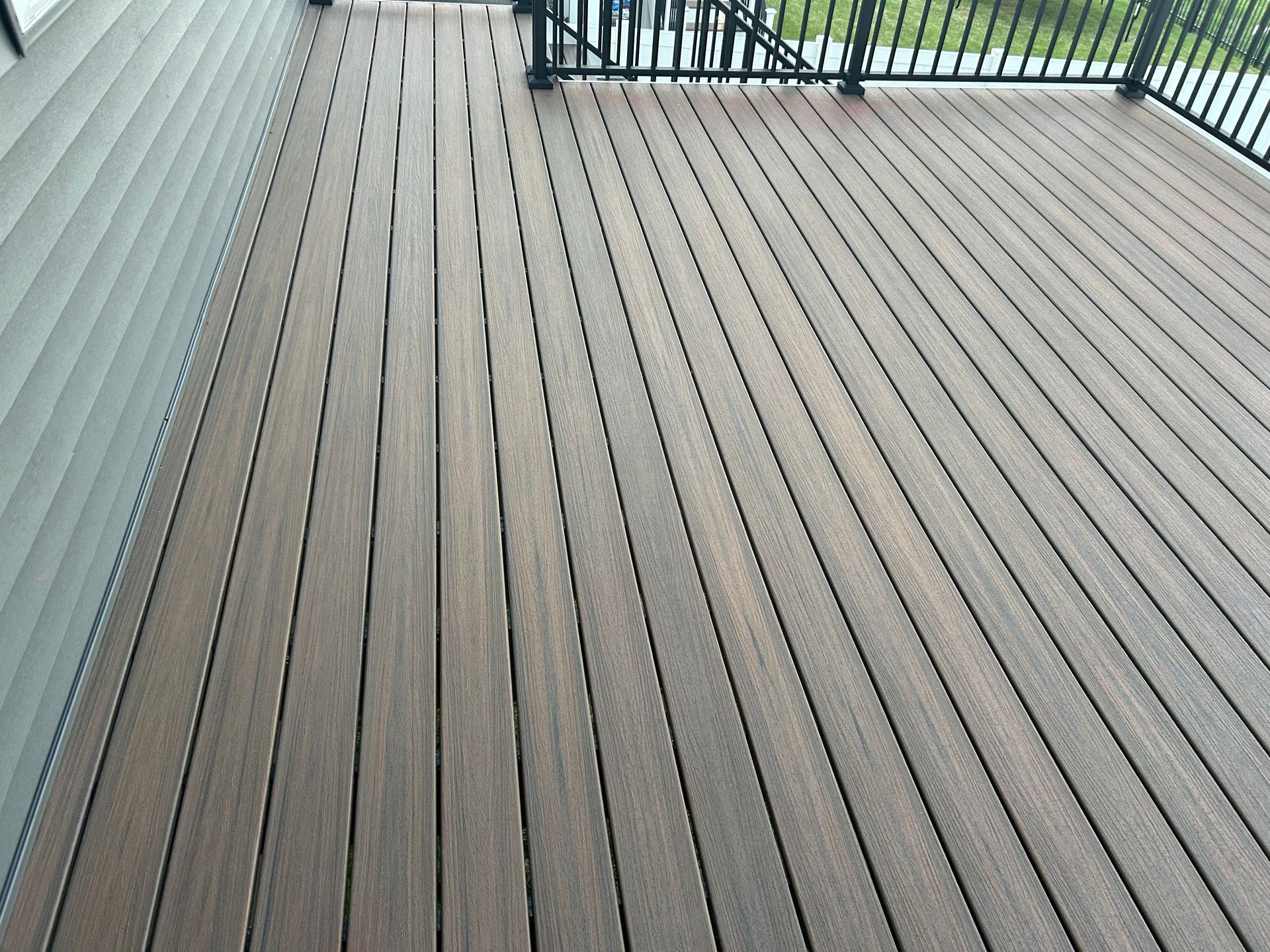A wooden deck with a black railing and a house in the background.